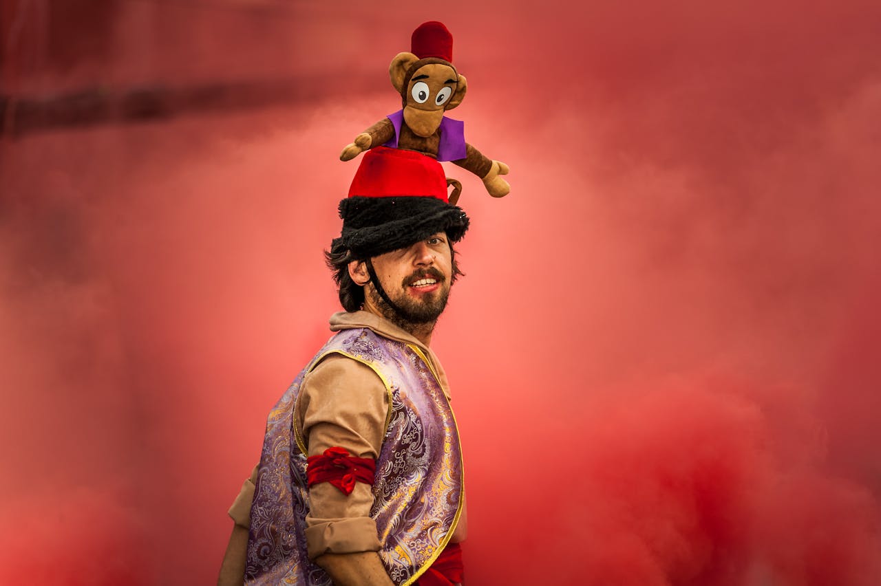 Man in colorful costume with a toy monkey on his hat amidst smoky red background.